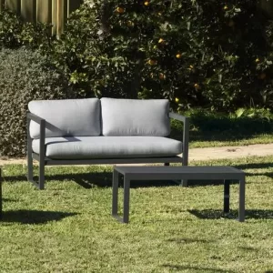 Mueble de exterior de jardín con un sofá de dos plazas ,dos sillones y una mesa de centro. El set de jardín está pintado en color gris.La imagen tiene platas en el fondo.